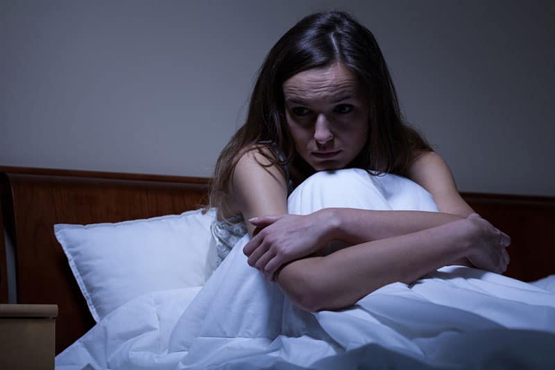worried woman sitting under blanket in bed