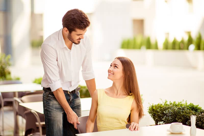 young man adjusting the chair of happy woman