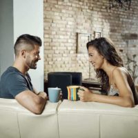 couple holding cup of tea and looking each other at home