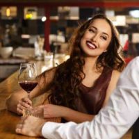mulher sorridente a segurar um copo de vinho num bar em frente a um homem