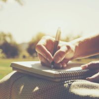 a woman is sitting in the park and writing something in a notebook