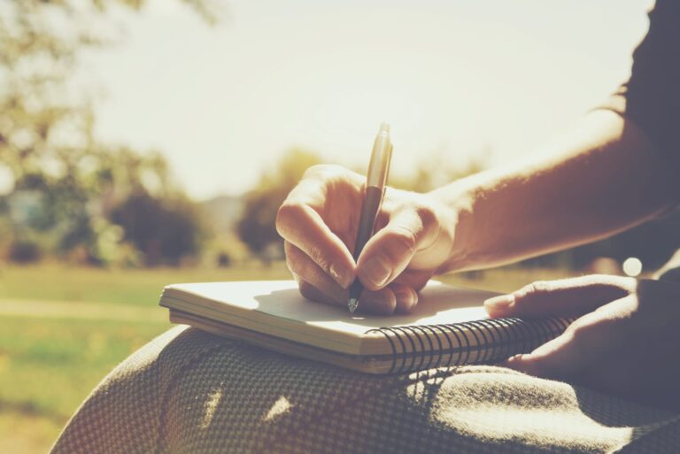 a woman is sitting in the park and writing something in a notebook