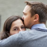 man kissing pensive woman in the forehead