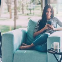 woman tying on phone whle sitting in sofa