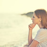 donna triste e pensierosa seduta sulla spiaggia da sola