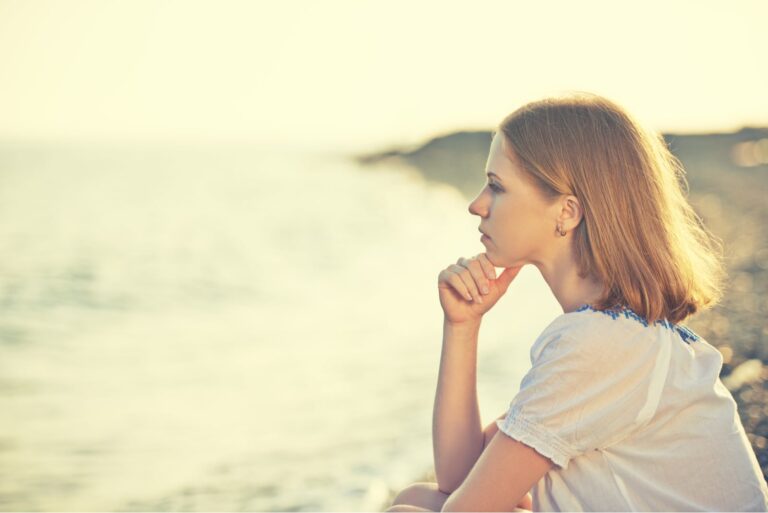 sad pensive woman sitting on the beach alone