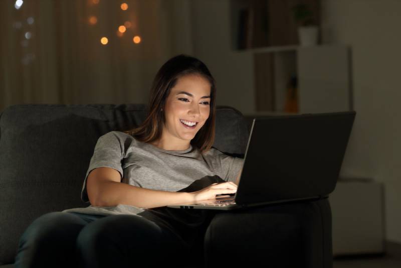Woman sitting a laptop at night sitting on a couch in the living room at home
