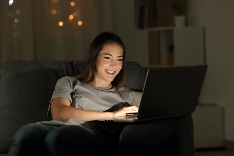 Woman sitting a laptop at night sitting on a couch in the living room at home