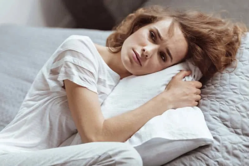 Worried woman lying on a pillow thinking about something depressing at home.