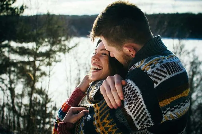 Young man in a sweater hugs a girl from behind