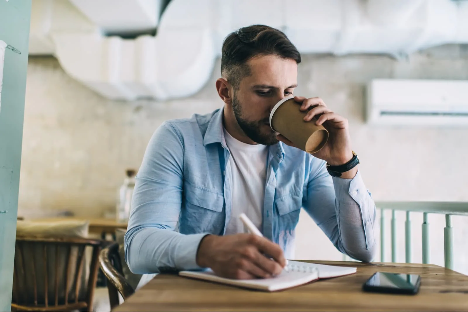 a man sits drinking coffee and writing