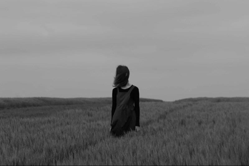 uma mulher com um vestido preto ao anoitecer está num campo de trigo