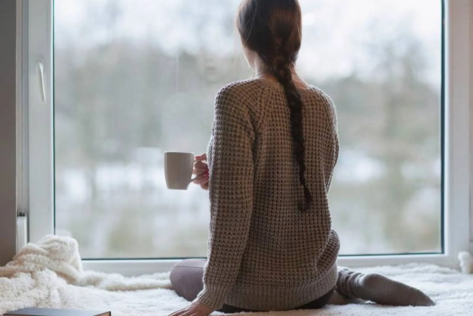 a woman is standing by the window with a cup of coffee