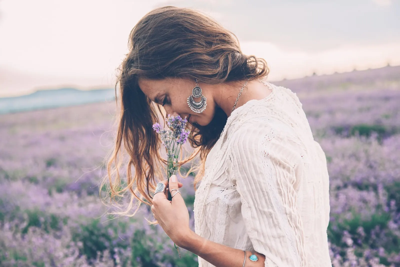 beautiful woman standing on flower field smelling flowers
