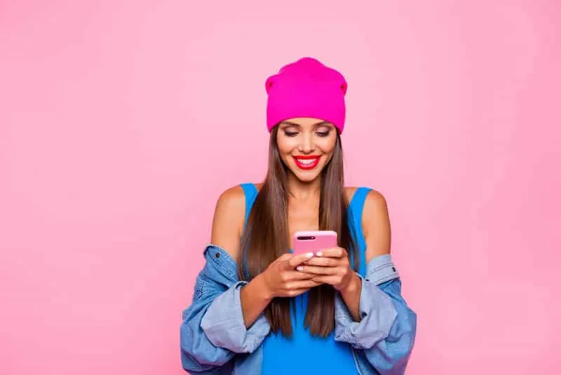 beautiful woman typing on her pink phone with pink background