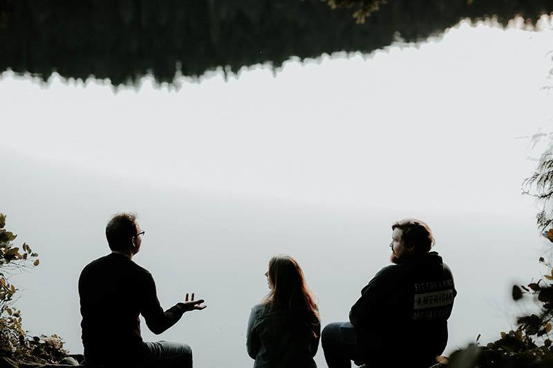 amigos sentados juntos à beira do lago