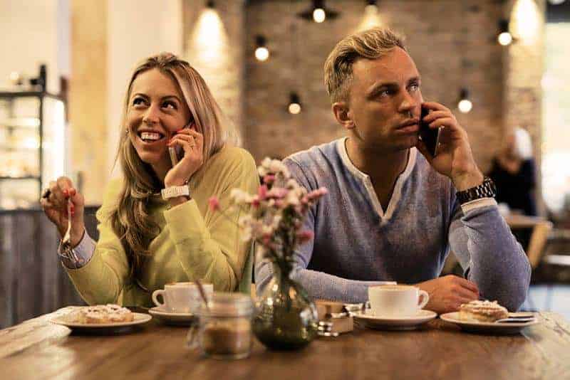 man and woman using their phone while sitting in restaurant
