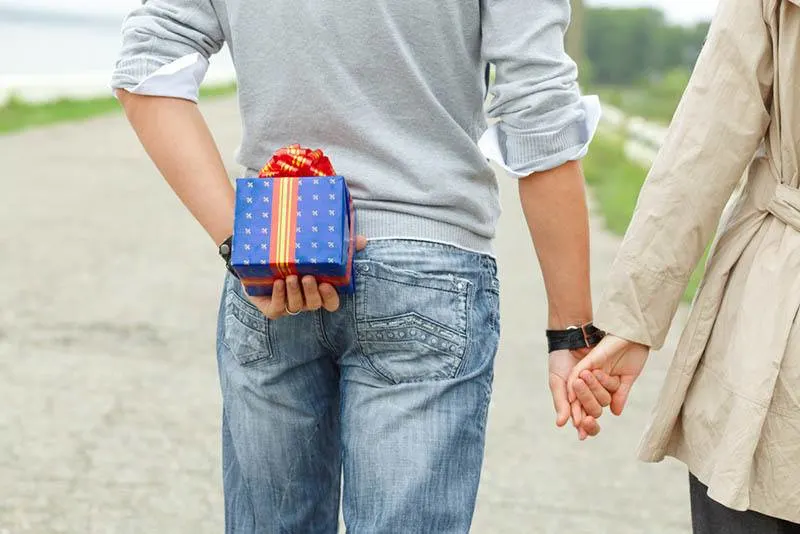 man holding gift behind while walking with girlfriend