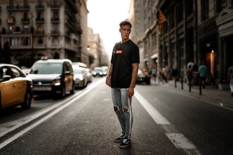 uomo in jeans blu e tshirt nera in piedi sulla strada vicino alle auto