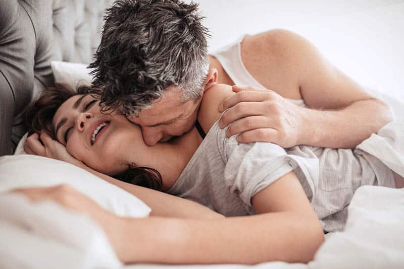 man kisses woman neck in bedroom