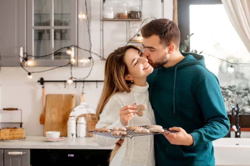 uomo che bacia la sua donna sulla guancia e tiene in mano dei biscotti