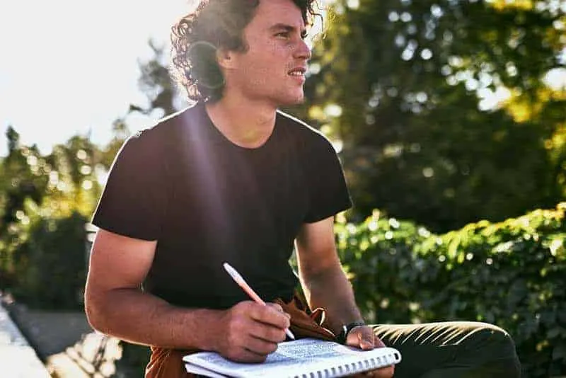 man writing on paper with pen outside