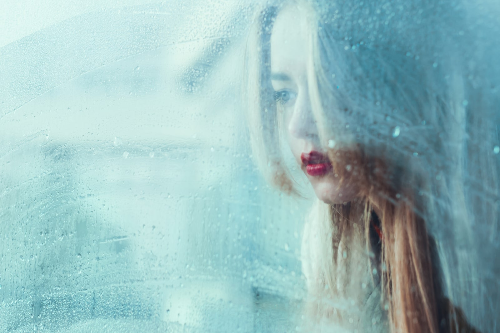 portrait of a beautiful young girl standing at the window watching the rain