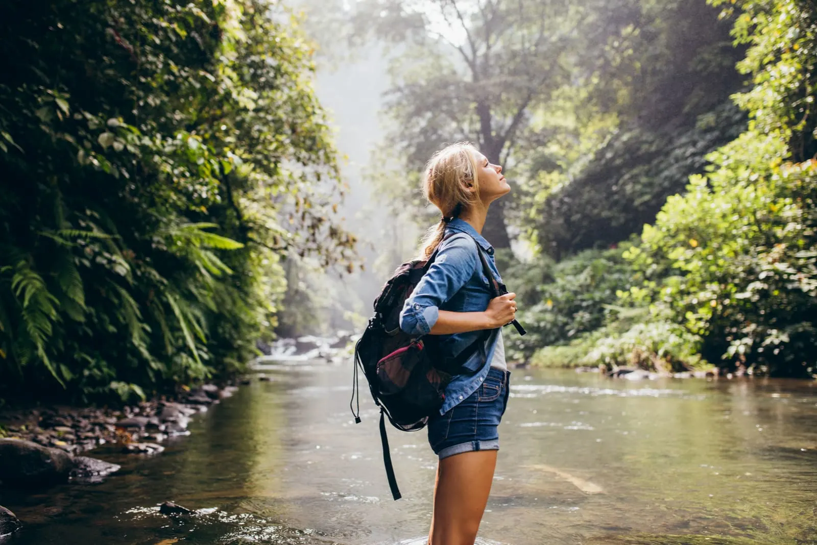 relaxed young woman with backpack standing by the stream