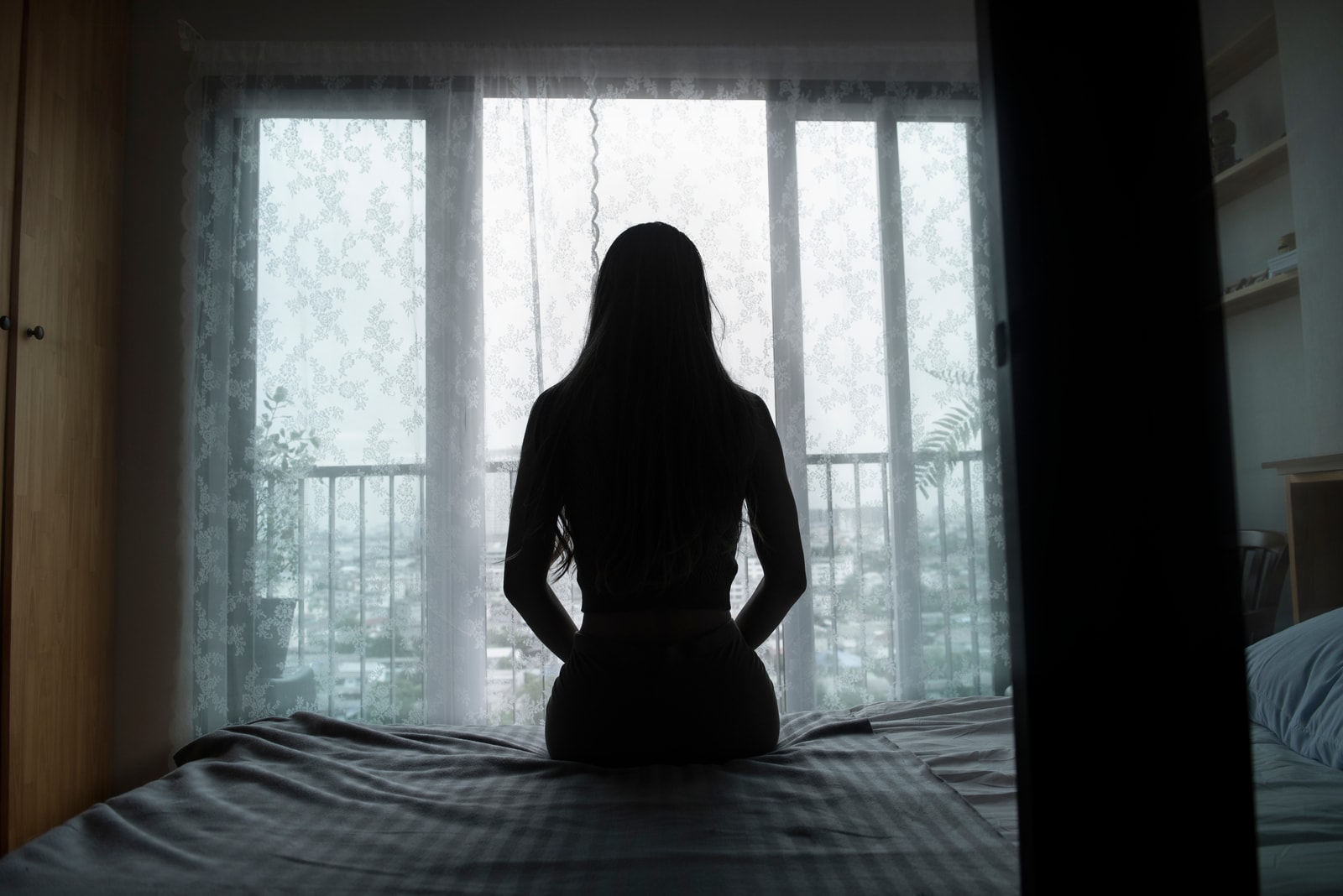 silhouette of a young woman sitting on a bed spending time alone at home