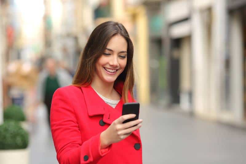 smiling woman looking at her phone on street