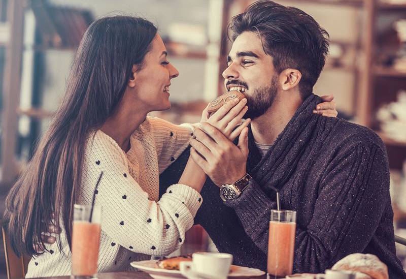 smiling woman putting cookie inside man mouth