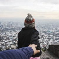 man holds woman's hand from back on city viewpoint