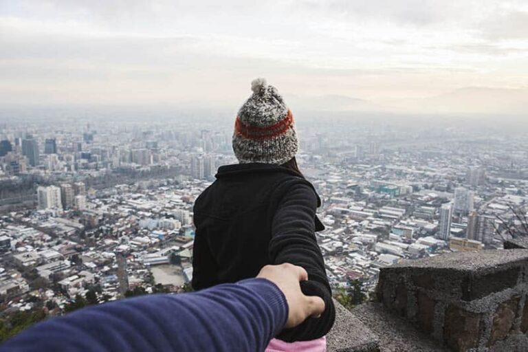 man holds woman's hand from back on city viewpoint