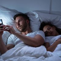 man typing on phone while woman sleeping