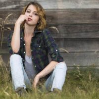 cute woman wearing black shirt sitting on grass and leaning on wood