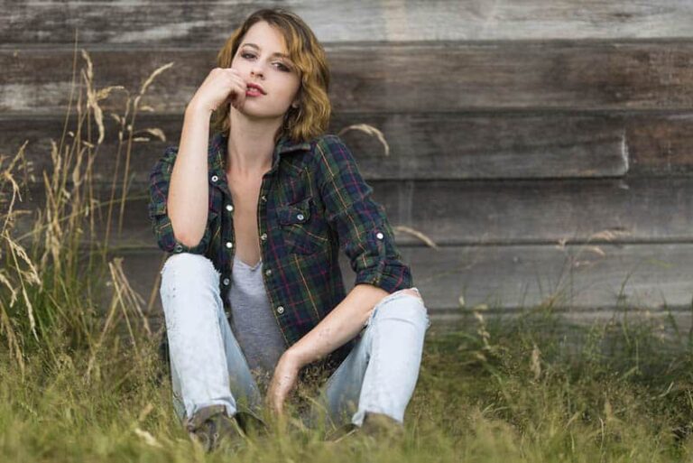 cute woman wearing black shirt sitting on grass and leaning on wood