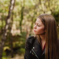 pensive woman wearing black jacket in forest