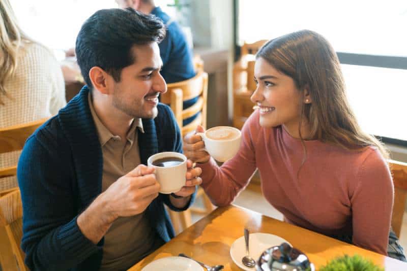 Jóvenes amantes disfrutan de un café mientras se miran en una cafetería