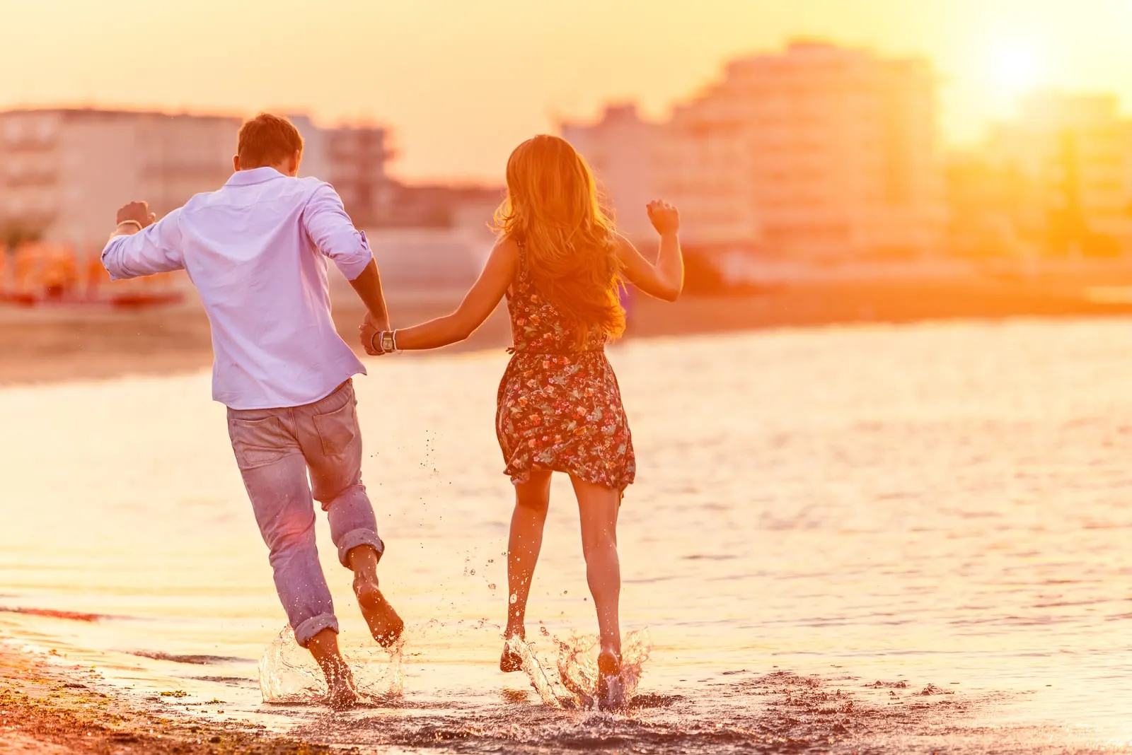 a loving couple holding hands and running across the shallows of the sea at sunset