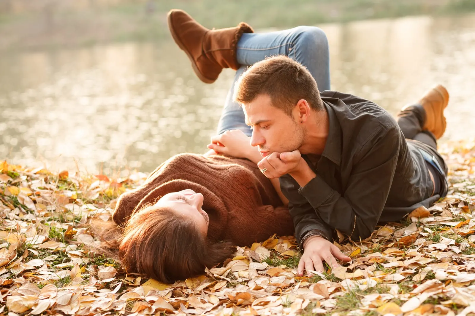 a man and a woman lie on dry leaves in autumn