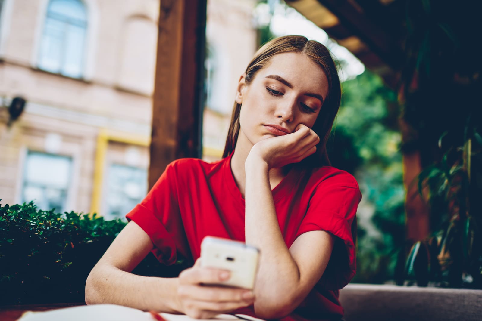 uma morena triste com uma t-shirt vermelha usa um smartphone