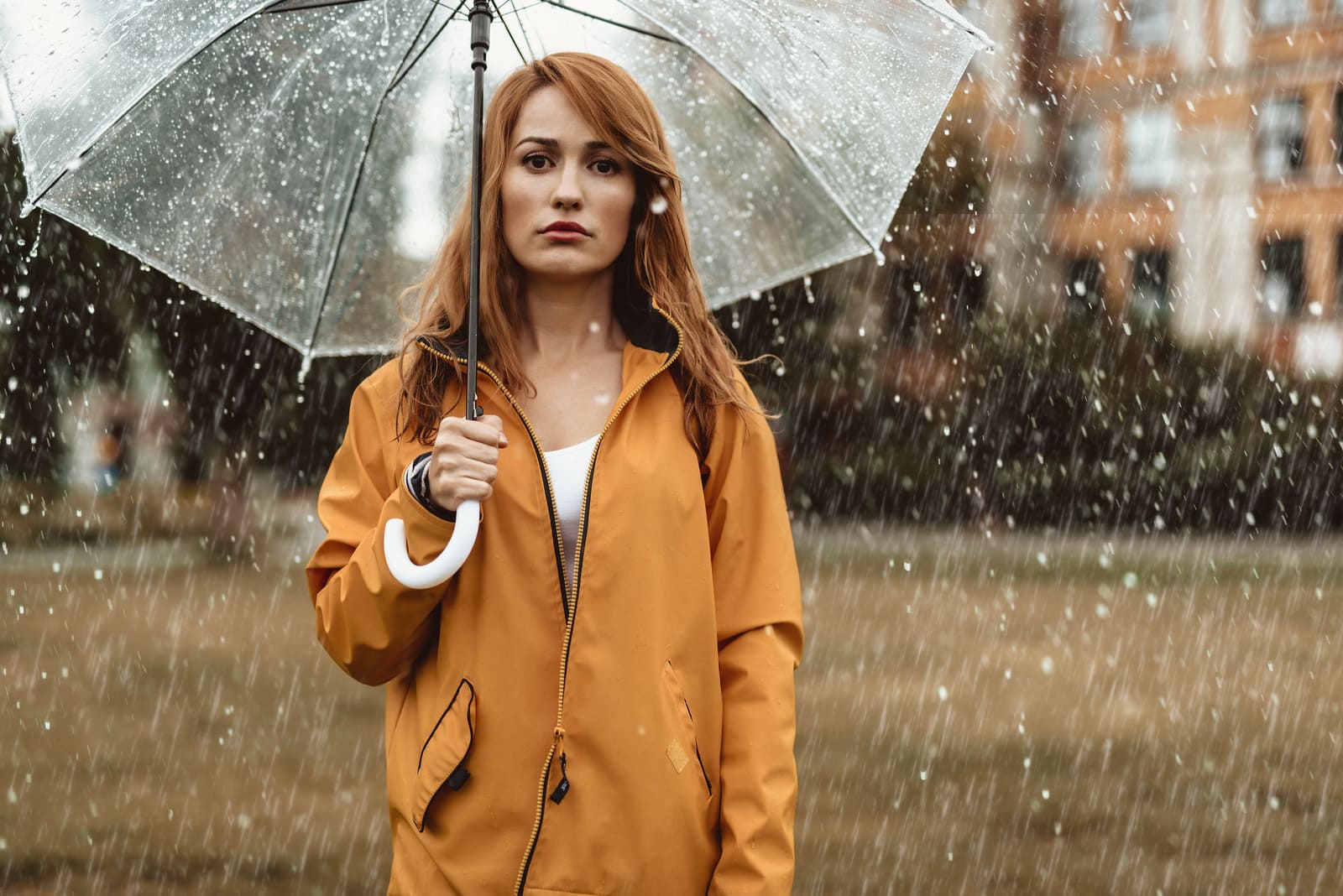 a woman in a yellow coat with an umbrella walks in the rain