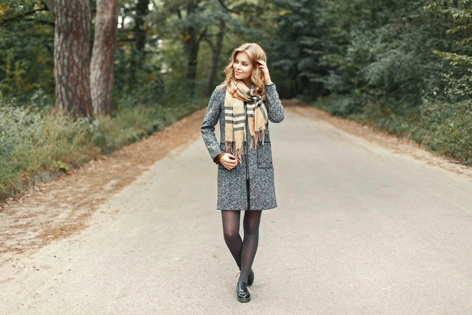 a woman with long brown hair in a gray coat stands in the street