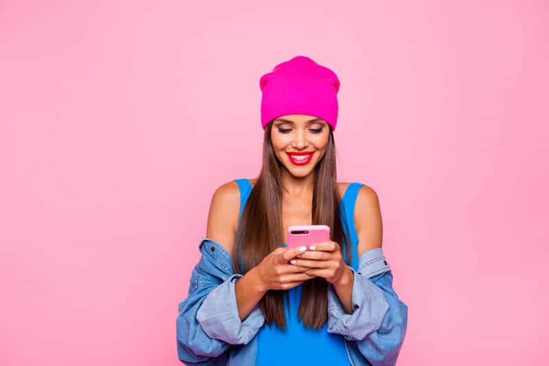 bella donna digitando sul suo telefono rosa con sfondo rosa