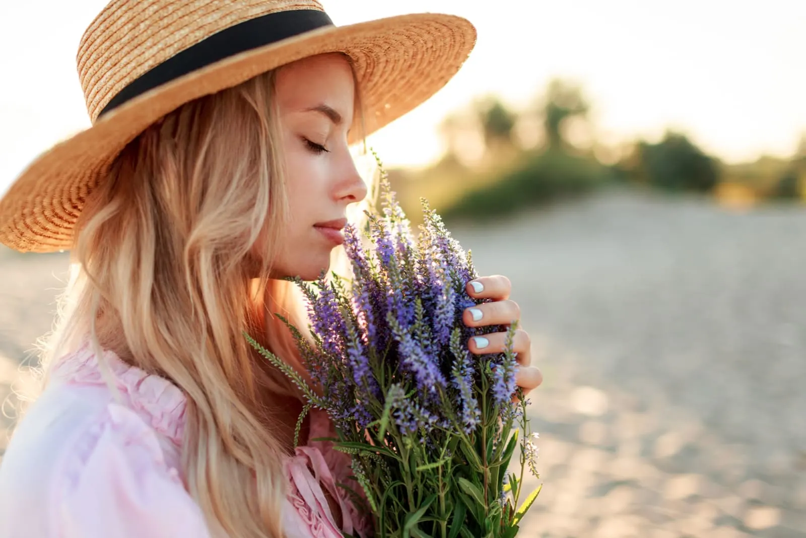 charming blonde girl in straw hat smells flowers on the beach