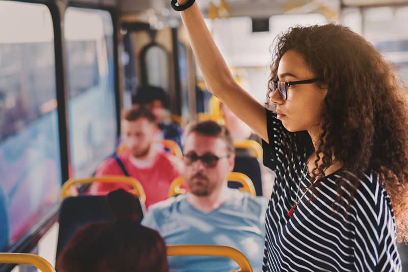 Kvinnan med lockigt hår som bär glasögon när hon står i kollektivtrafiken