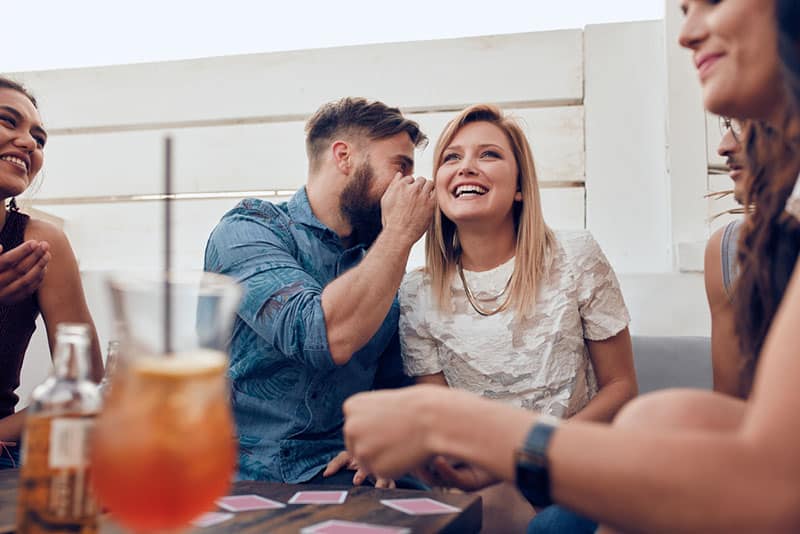 man whispering to woman around friends