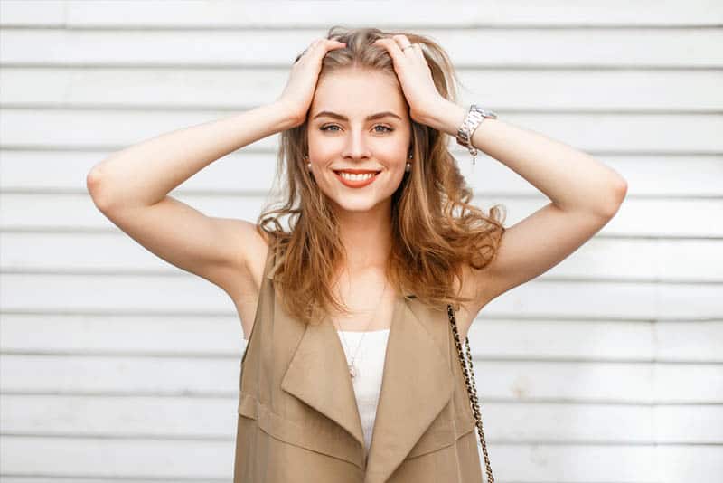 retrato de uma rapariga loira sorridente com as mãos na cabeça