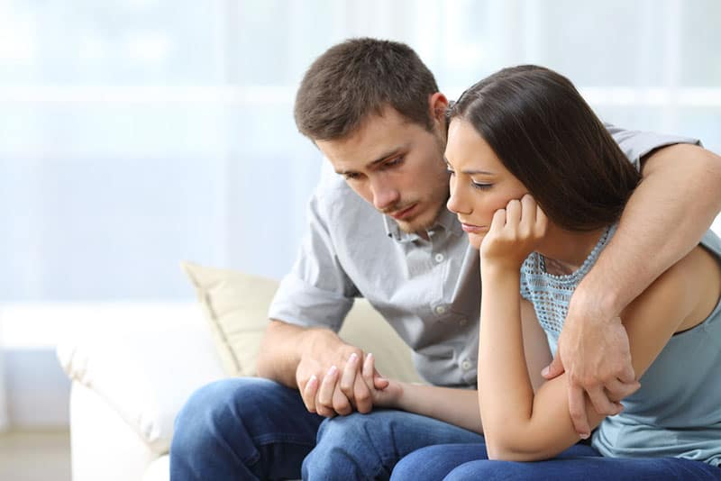 coppia triste seduta a casa, uomo che conforta la donna