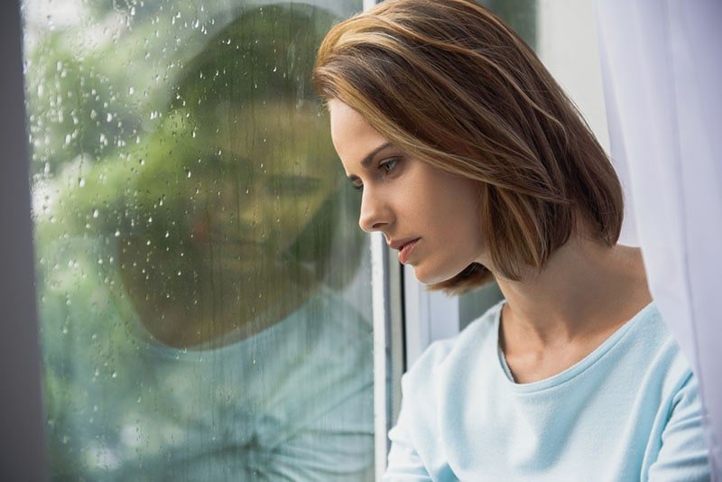 mulher triste a olhar através de uma janela chuvosa